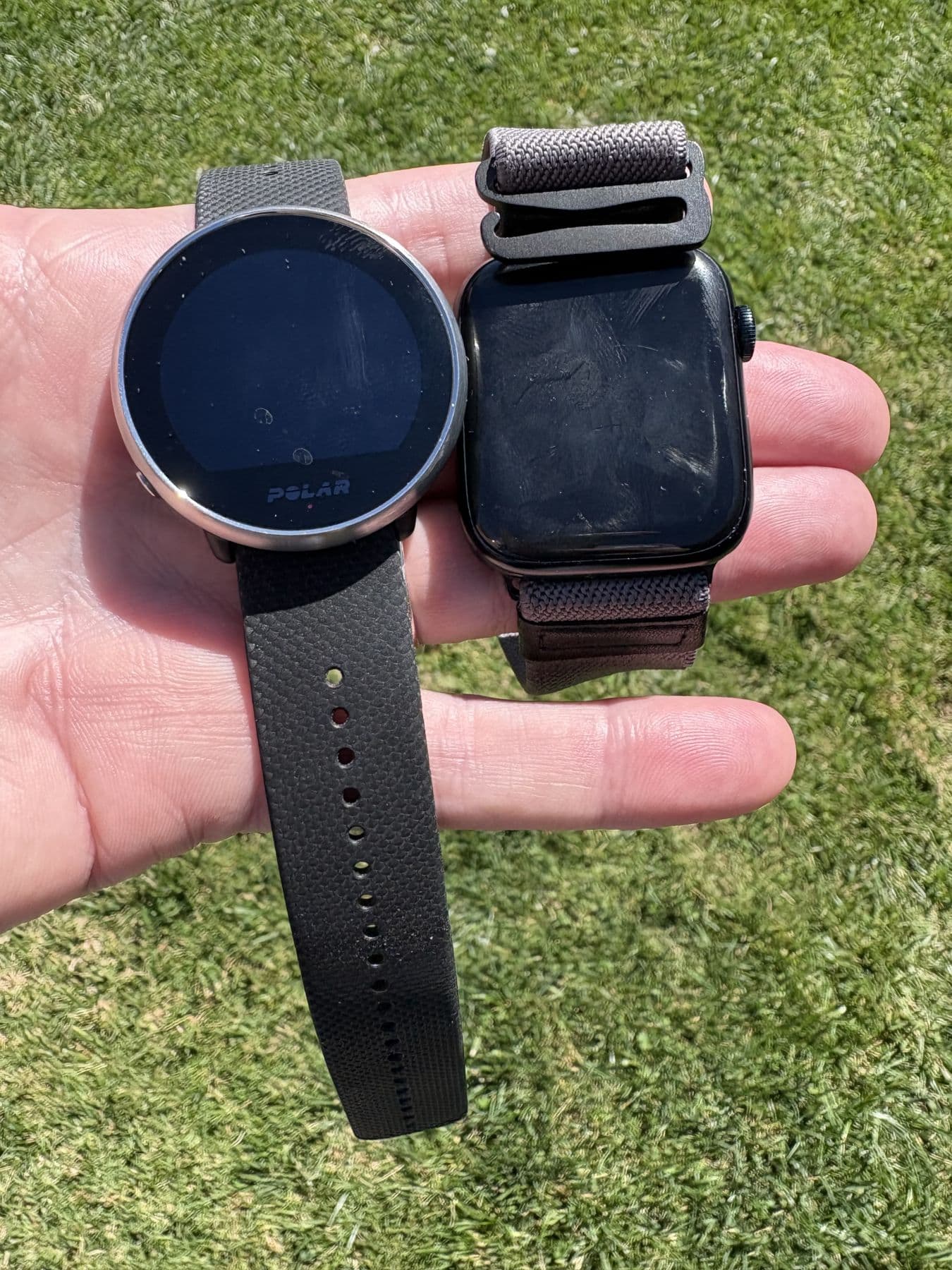 Hand holding a round Polar sports watch and a square smartwatch over grass